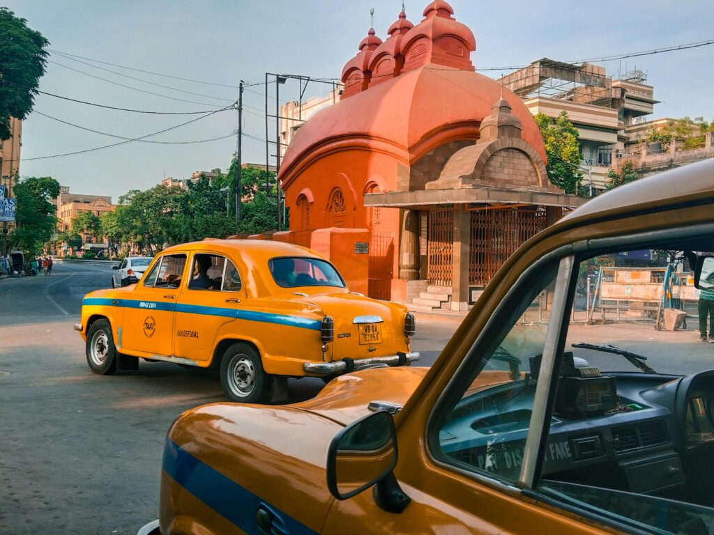 Classic Kolkata yellow taxis by a traditional temple, capturing urban India's vibrant culture.