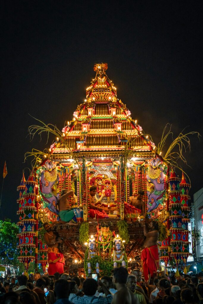 Vibrant nighttime festival featuring an illuminated, decorated float surrounded by people, creating a lively atmosphere.