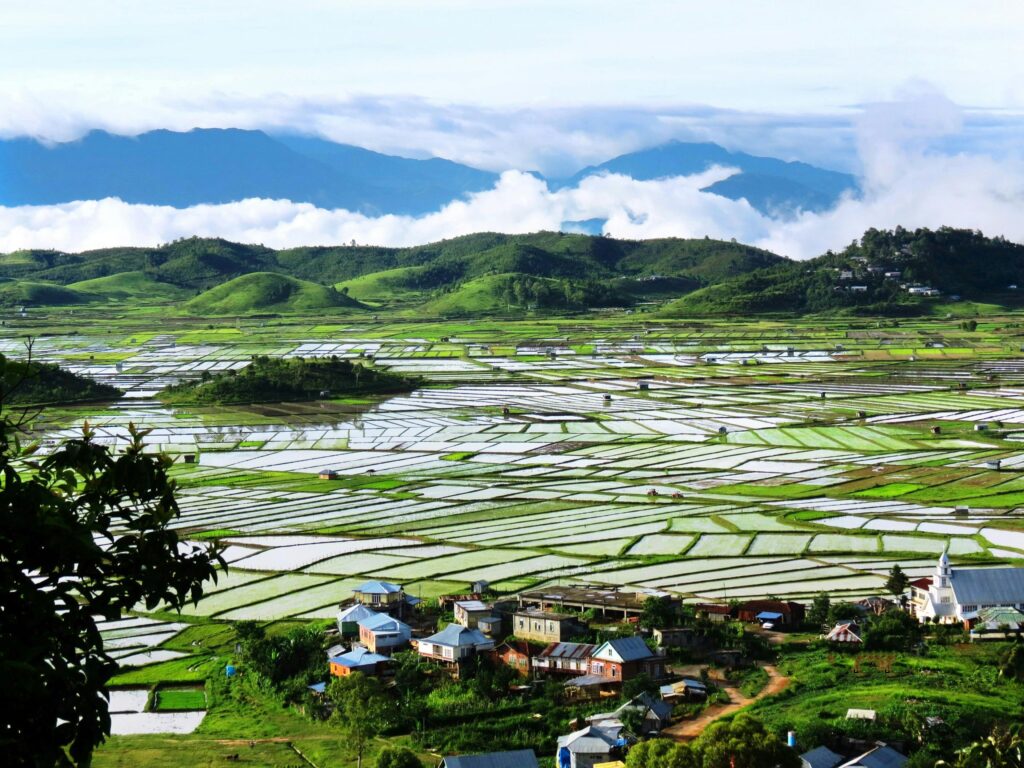 A stunning birds-eye view of rice fields and a rural village with mountainous backdrop.